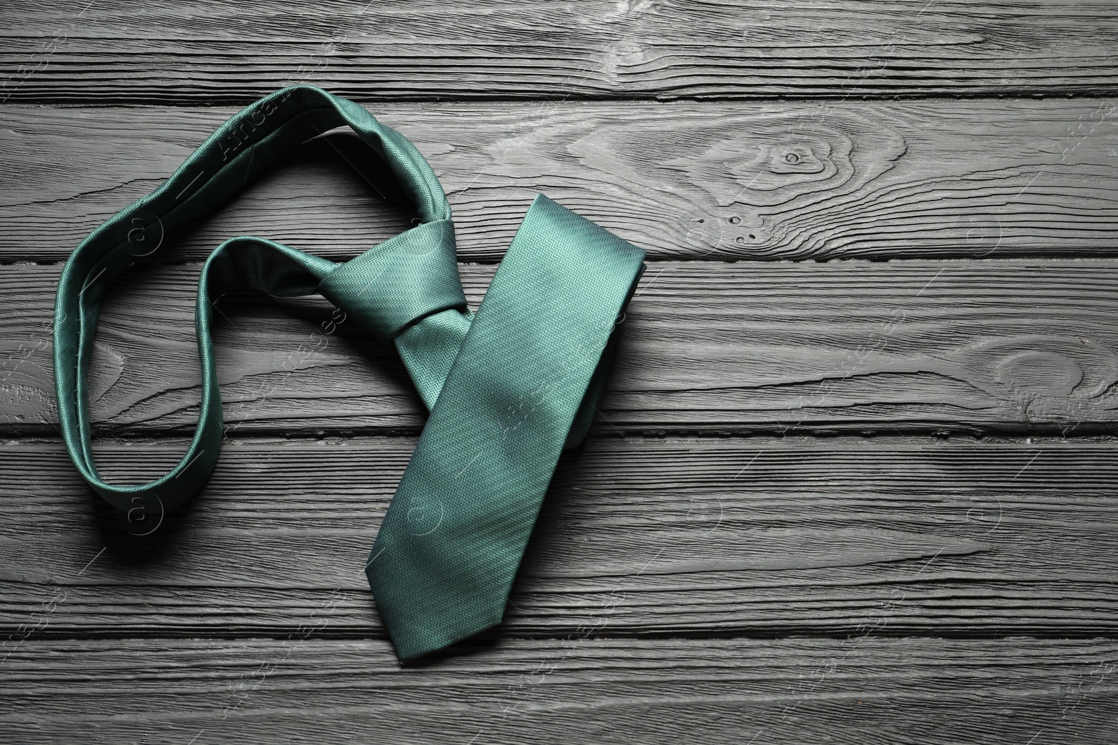 Photo of One green necktie on black wooden table, top view. Space for text