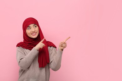 Photo of Muslim woman in hijab pointing at something on pink background, space for text