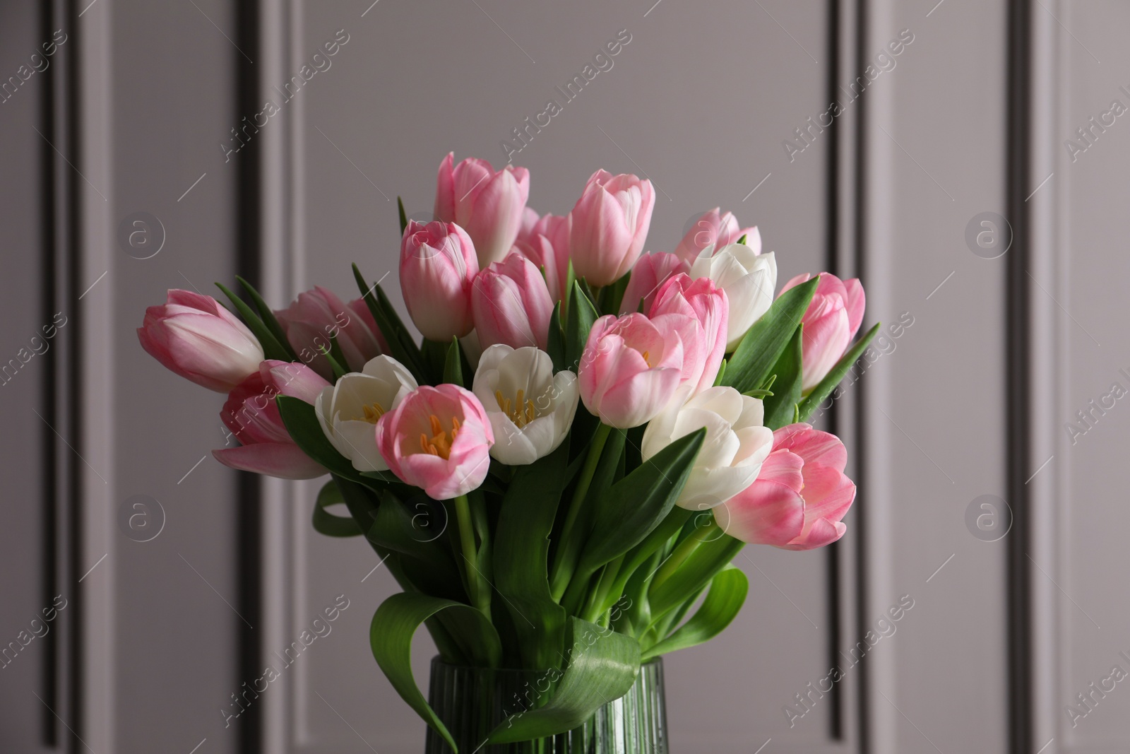 Photo of Beautiful bouquet of tulips in glass vase against grey wall