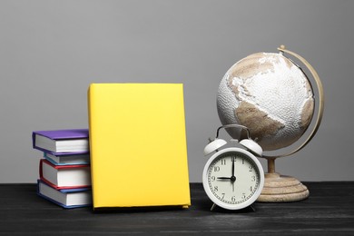 Photo of Different books, globe and alarm clock on black wooden table against gray background