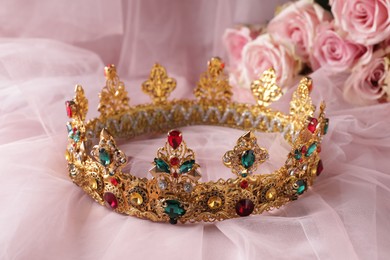 Photo of Beautiful golden crown with gems on pink cloth