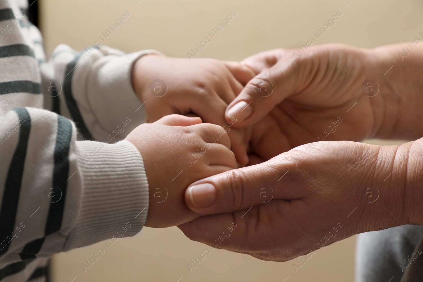 Photo of Woman holding hands with her granddaughter on beige background, closeup