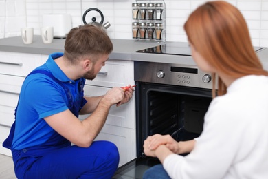 Housewife with repairman near modern oven in kitchen