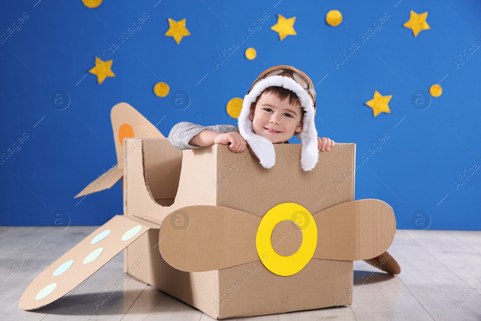 Photo of Cute little child playing with cardboard airplane near blue wall