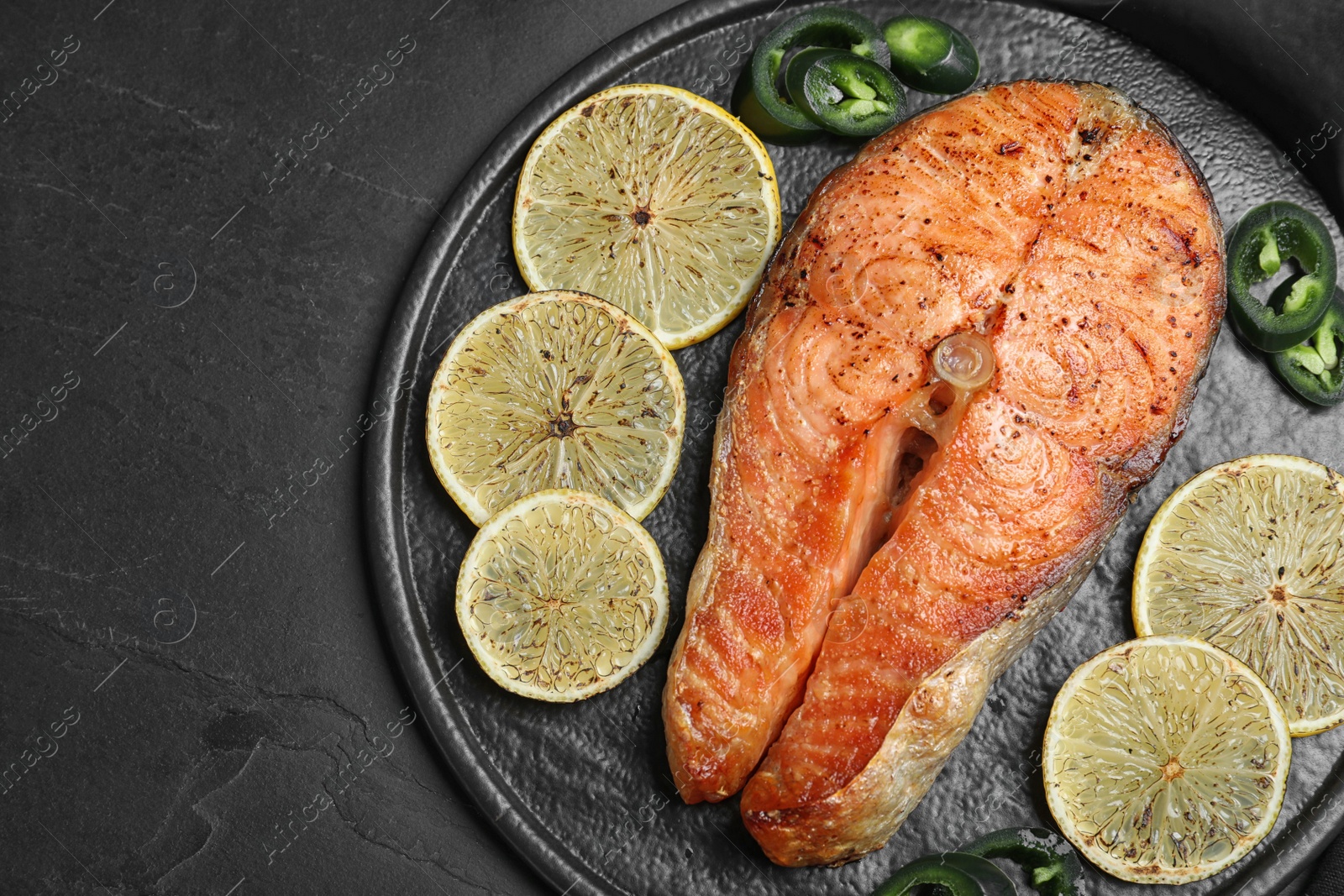 Photo of Delicious roasted fish served on black table, top view