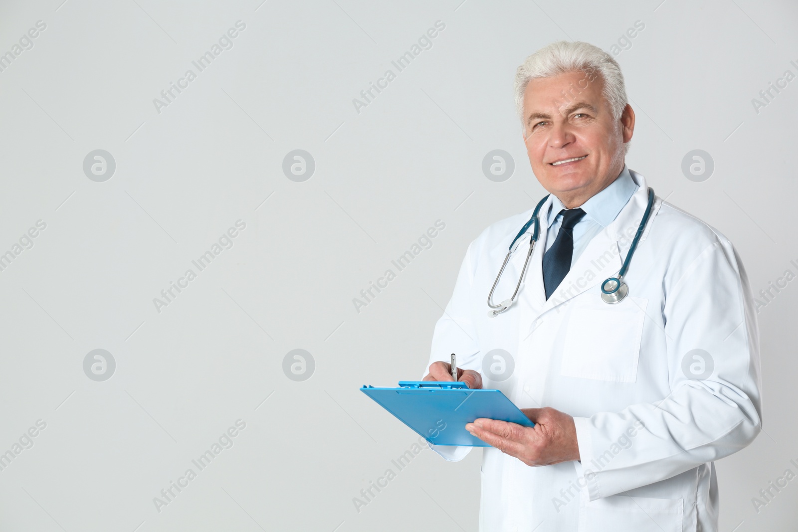 Photo of Portrait of senior doctor with clipboard against light background