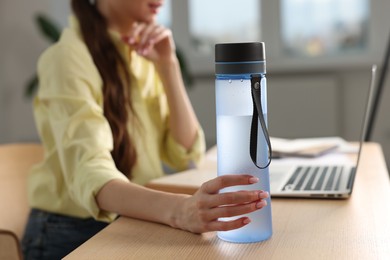 Photo of Woman holding transparent bottle at workplace indoors, closeup