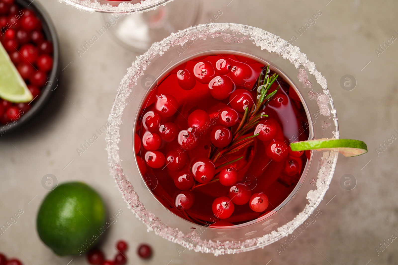 Photo of Tasty cranberry cocktail with rosemary and lime in glass on grey table, flat lay