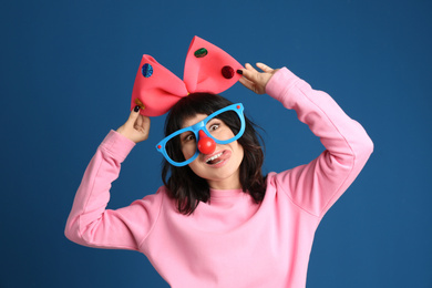 Photo of Emotional woman with funny glasses and large bow on blue background. April fool's day