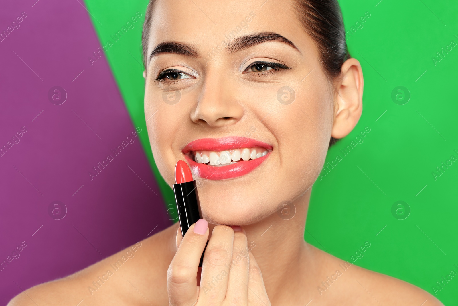 Photo of Young woman applying lipstick on color background