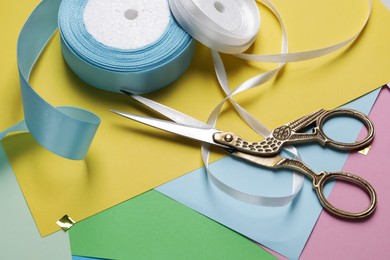 Photo of Beautiful scissors near ribbon on colorful paper sheets, closeup