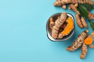 Whole and cut turmeric roots on light blue wooden table, flat lay. Space for text