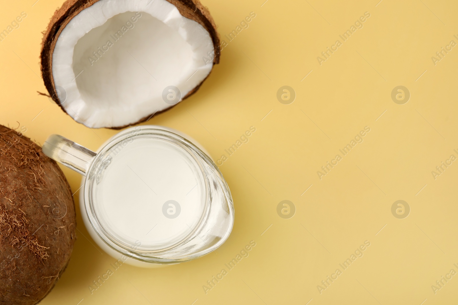 Photo of Glass jug of delicious vegan milk and coconuts on yellow background, flat lay. Space for text