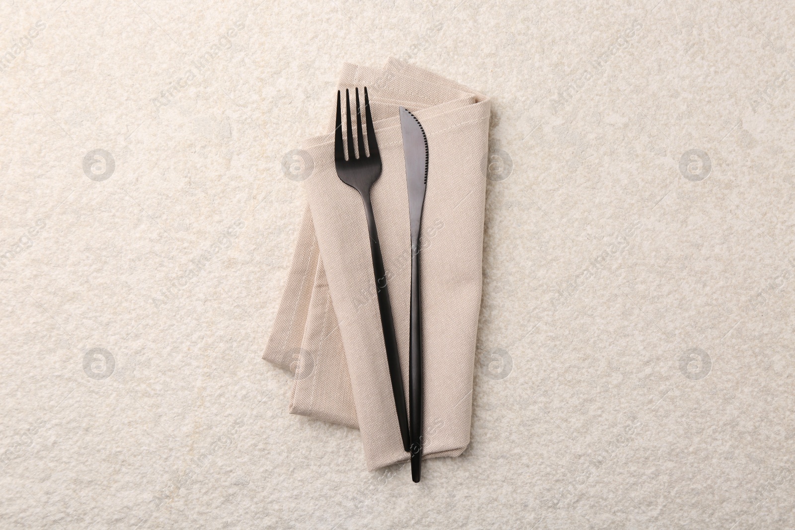 Photo of Stylish cutlery and dinner napkin on beige textured table, top view