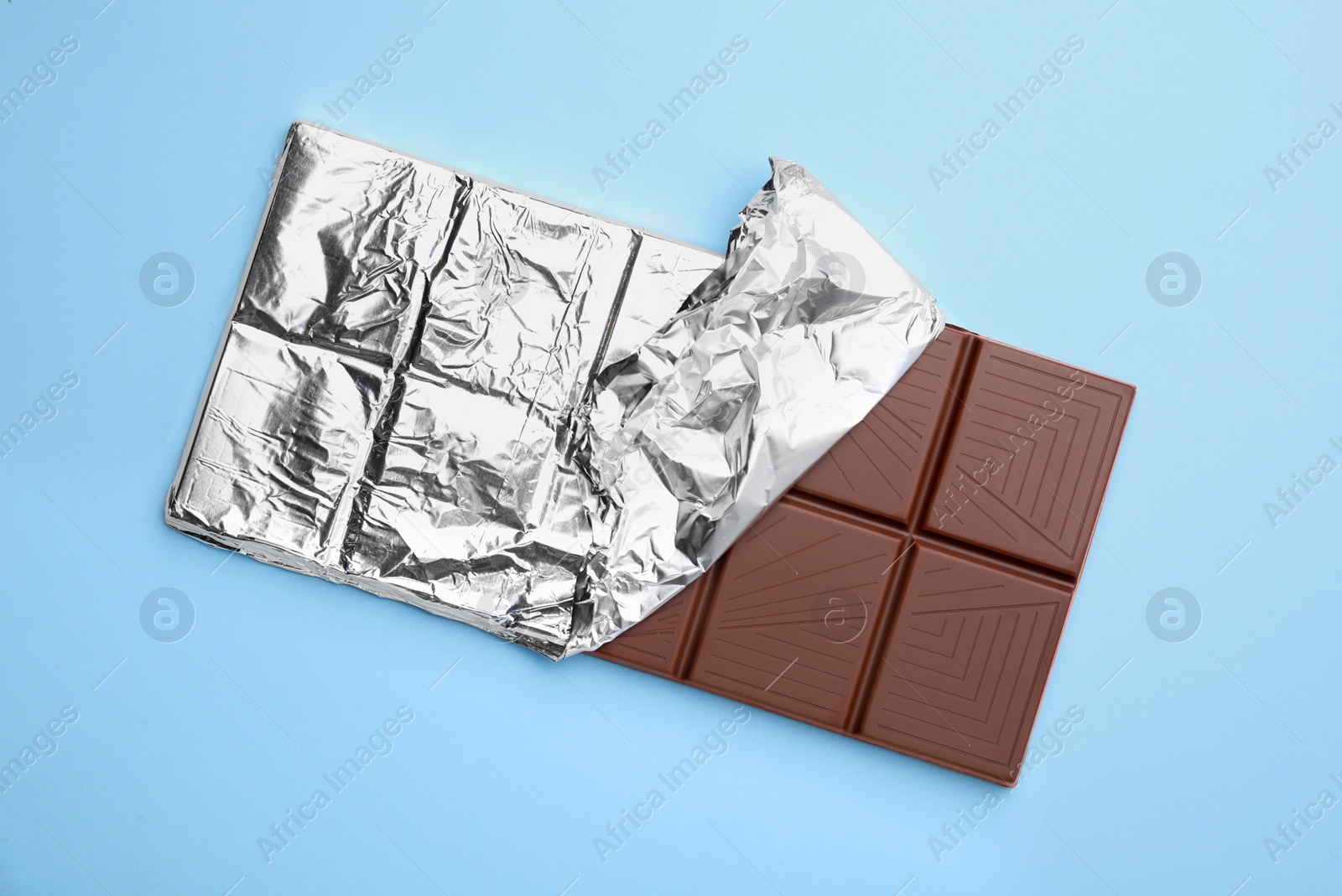 Photo of Tasty chocolate bar on light blue background, top view