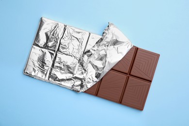 Photo of Tasty chocolate bar on light blue background, top view