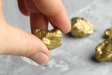 Photo of Woman holding gold nugget at grey textured table, closeup. Space for text