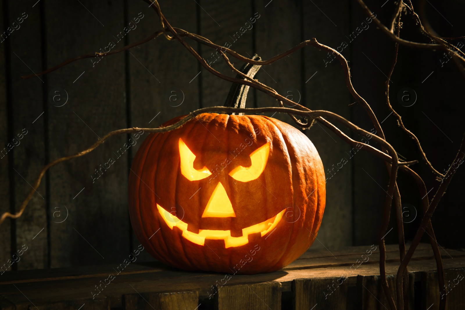 Photo of Scary jack o'lantern pumpkin on wooden bench in darkness. Halloween decor