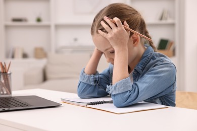 Little girl suffering from headache while doing homework at home