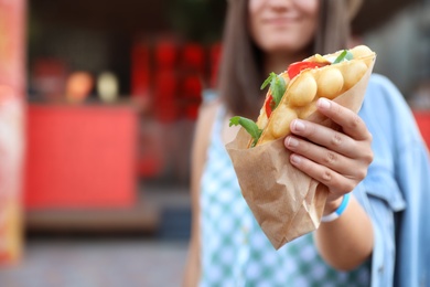 Young woman holding delicious bubble waffle with tomato and arugula outdoors, closeup