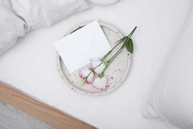 Photo of Tray with beautiful flowers and envelope on white bed, top view