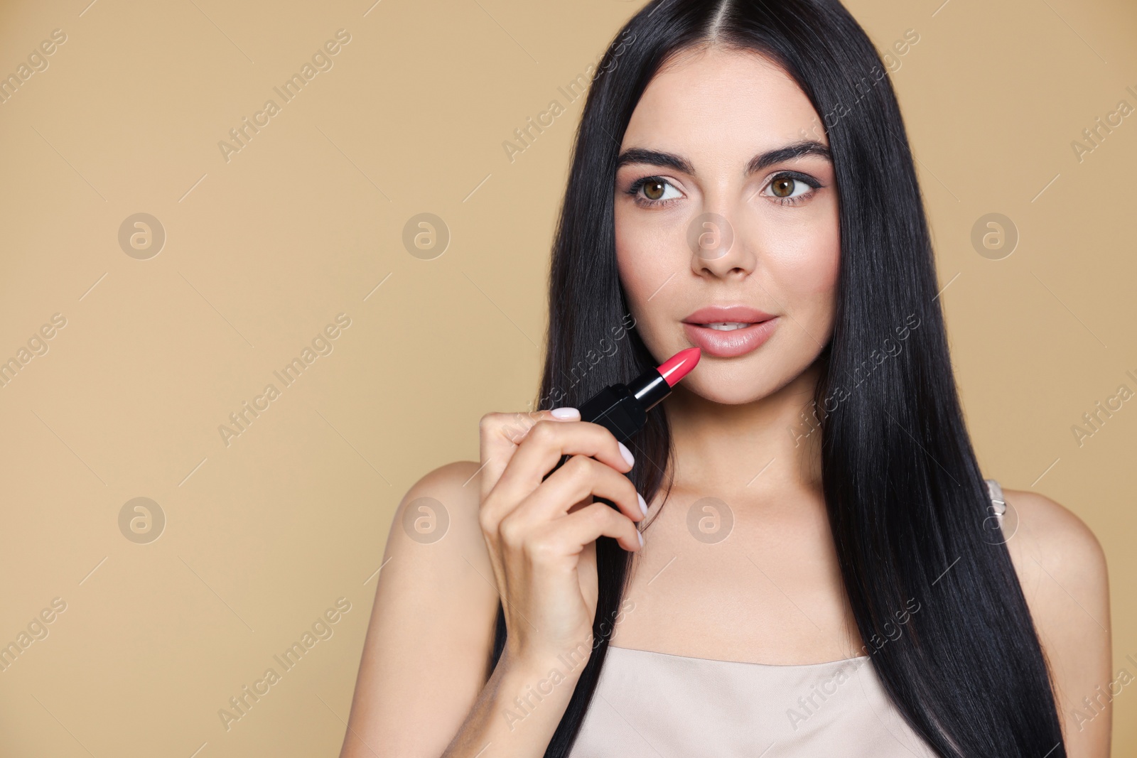 Photo of Young woman with beautiful makeup holding nude lipstick on beige background, space for text