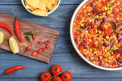 Delicious chili con carne served on wooden table, flat lay