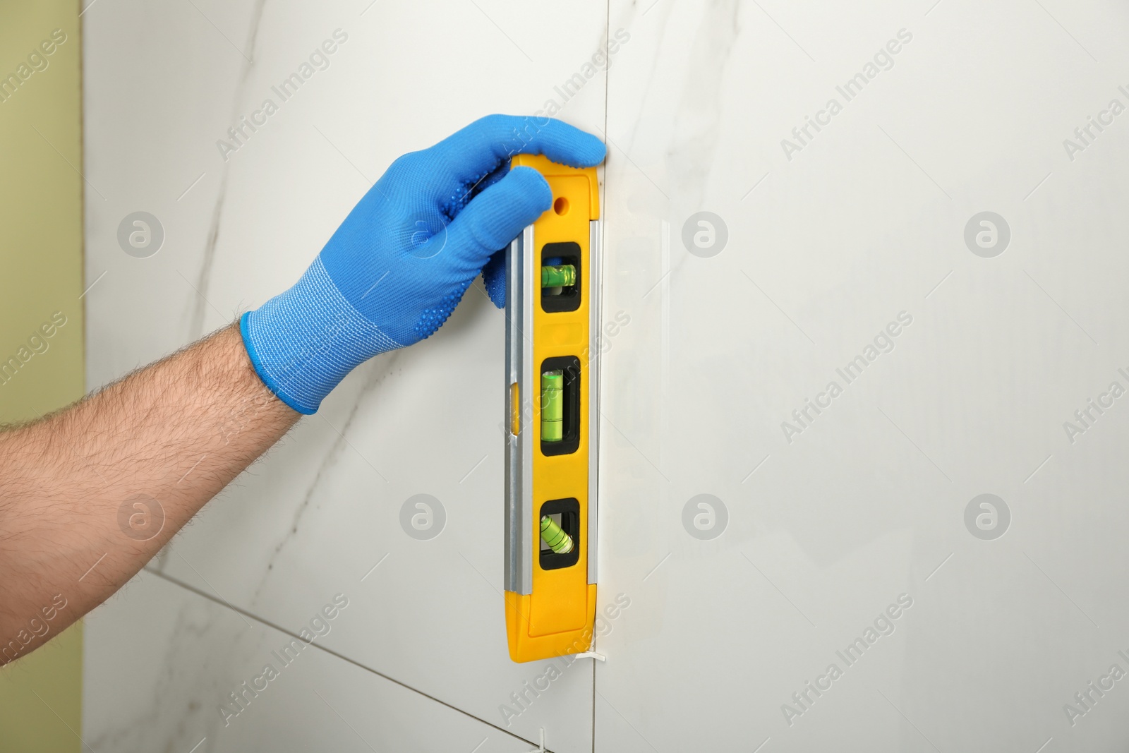 Photo of Man checking proper ceramic tile installation with level on wall, closeup. Building and renovation works