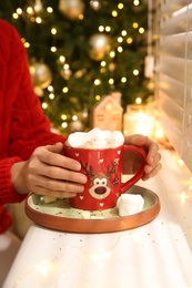 Photo of Woman with delicious marshmallow cocoa near window indoors, closeup. Christmas celebration