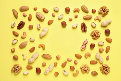 Photo of Different delicious nuts on yellow background, flat lay. Space for text