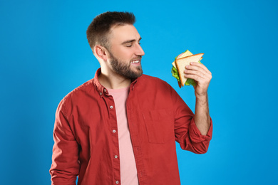 Young man with tasty sandwich on light blue background