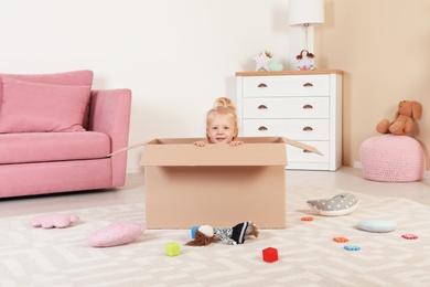 Cute little girl playing with cardboard box at home