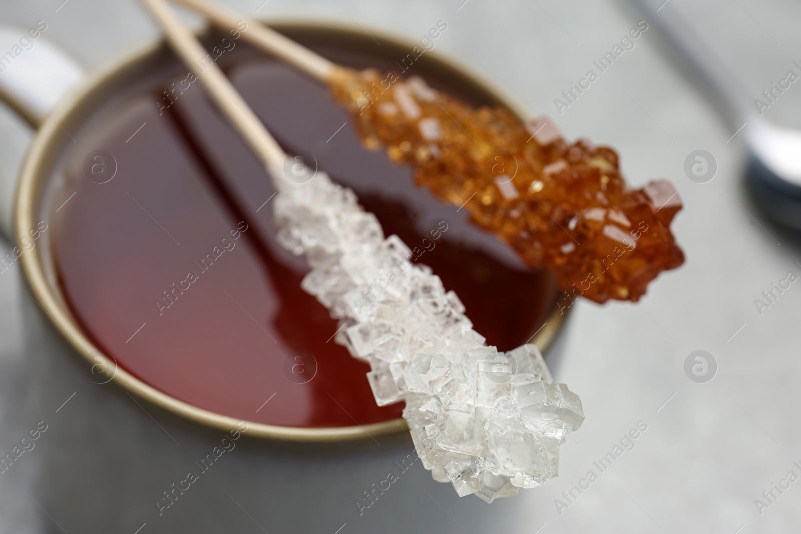 Photo of Sticks with sugar crystals and cup of tea on table, closeup