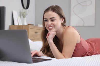 Photo of Happy woman with laptop on bed in bedroom