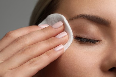 Photo of Beautiful woman removing makeup with cotton pad on grey background, closeup