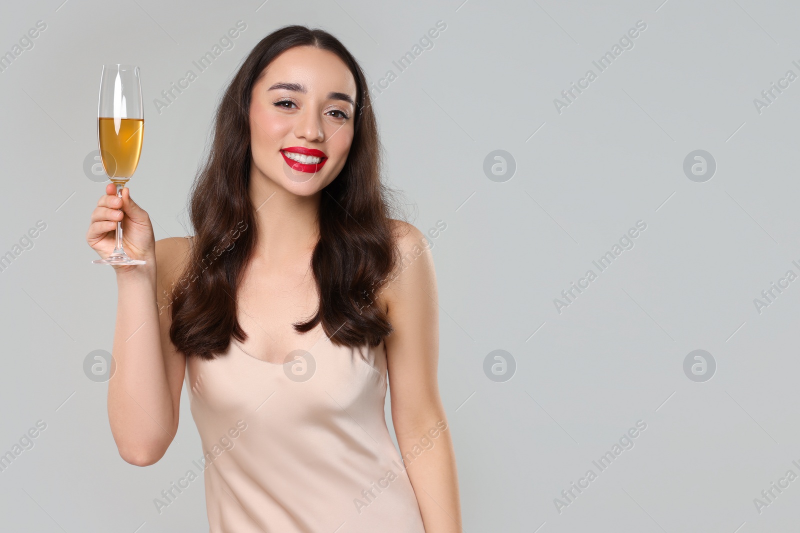 Photo of Christmas celebration. Beautiful young woman with glass of champagne on grey background, space for text