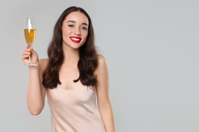 Photo of Christmas celebration. Beautiful young woman with glass of champagne on grey background, space for text