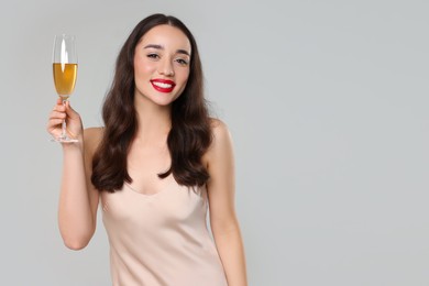 Christmas celebration. Beautiful young woman with glass of champagne on grey background, space for text