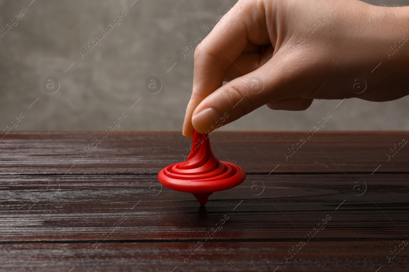 Photo of Woman playing with red spinning top at wooden table, closeup