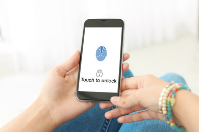 Image of Woman holding smartphone with fingerprint sensor indoors, closeup. Digital identity