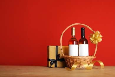 Bottles of wine in wicker basket with bow and gift on table against color background. Space for text