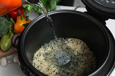 Pouring water into multi cooker with rice, closeup