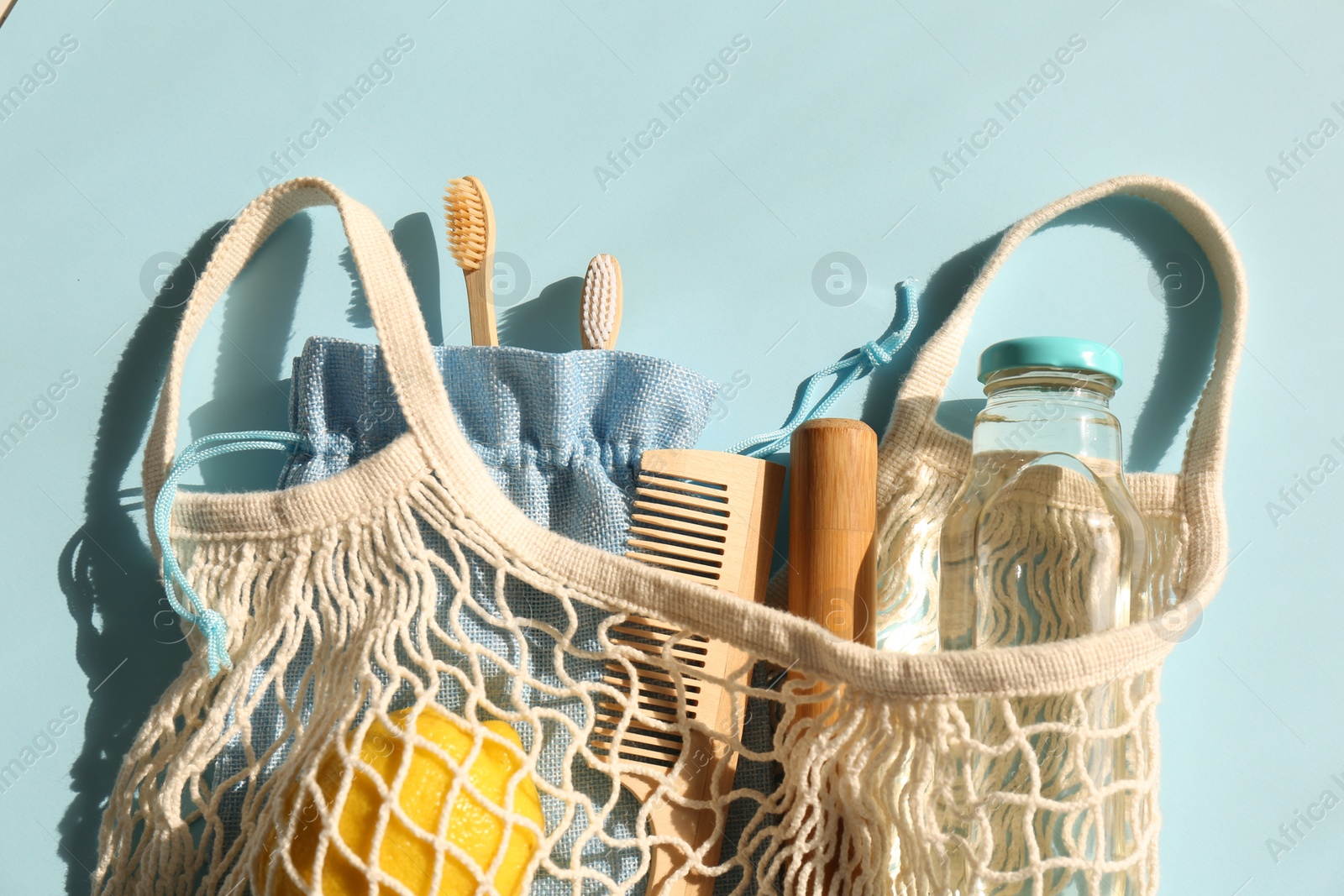 Photo of Fishnet bag with different items on light blue background, top view. Conscious consumption