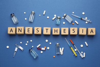 Photo of Word Anesthesia made of wooden cubes and drugs on blue background, flat lay