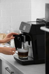 Woman using modern espresso machine for making coffee with milk in kitchen, closeup