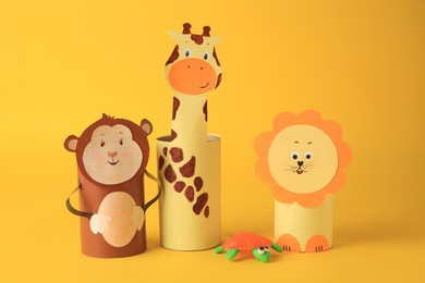 Photo of Toy monkey, giraffe and lion made from toilet paper hubs with plasticine turtle on yellow background. Children's handmade ideas