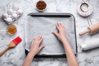 Photo of Woman putting parchment paper in baking pan at white marble table, top view