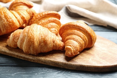 Photo of Board with tasty croissants on dark wooden table, closeup. French pastry