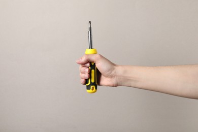 Woman holding screwdriver on grey background, closeup