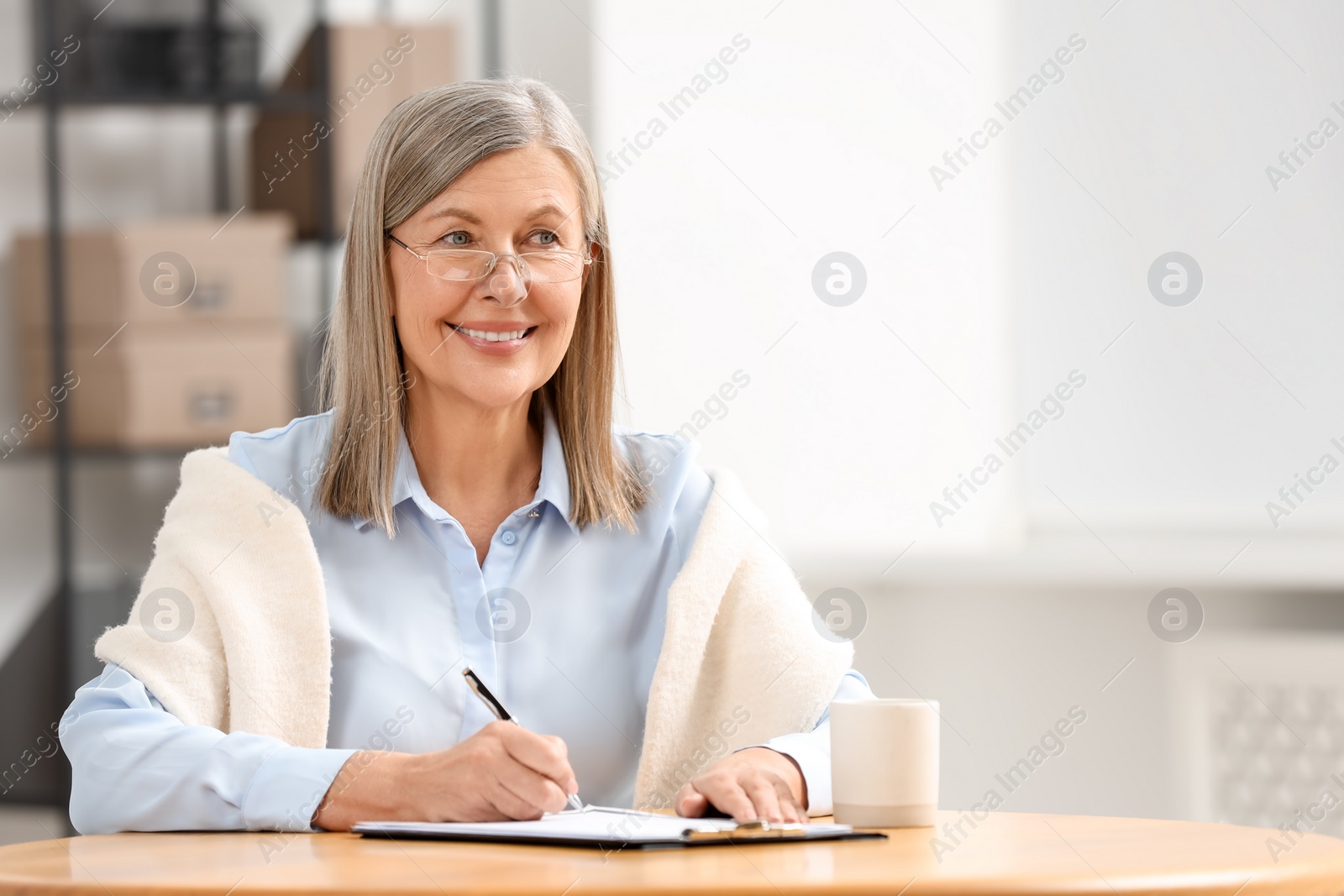 Photo of Smiling senior woman signing Last Will and Testament at table indoors. Space for text